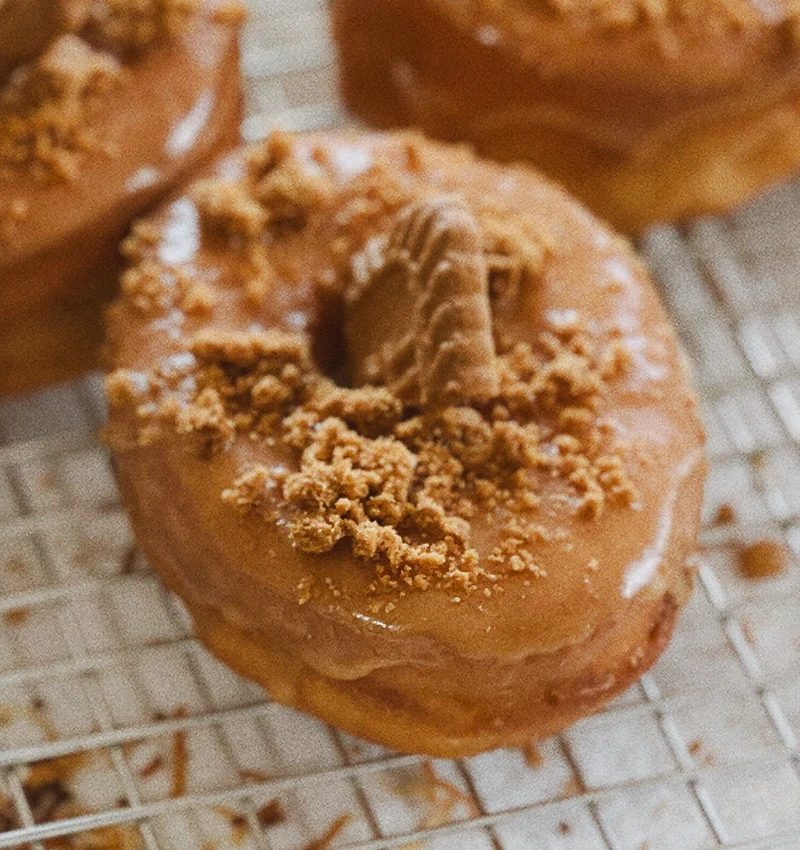 Belgian Crush doughnuts with Biscoff glaze, cookie pieces and crumble on a cooling rack